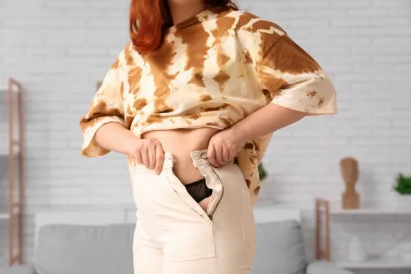 Image of woman trying to do her trousers up after pregnancy weight gain Warrington