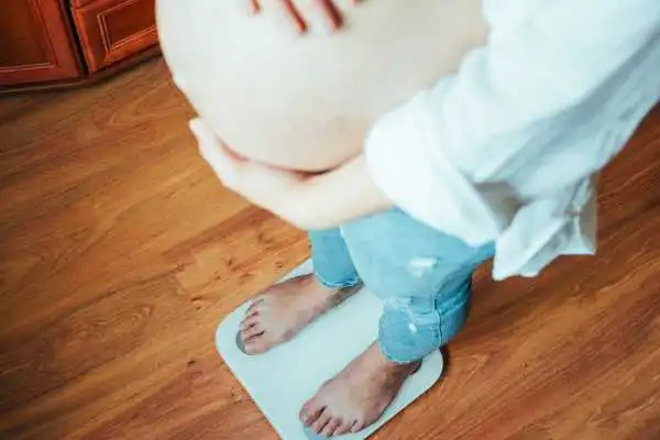 Image of woman weighing herself and experiencing weight gain through pregnancy Warrington